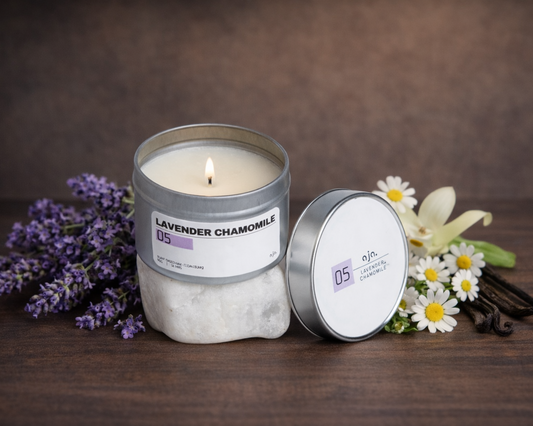 Candle in a decorative tin with lavender, chamomile flowers, and vanilla on a wooden surface.