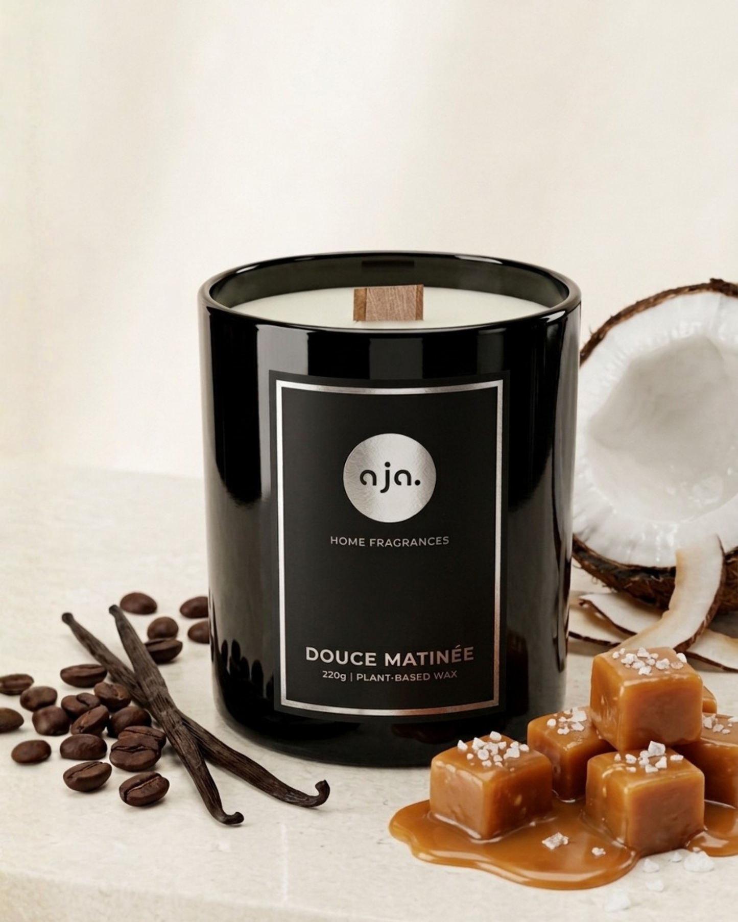Black candle labeled 'aja' with vanilla beans, coffee beans, and coconut on a light background