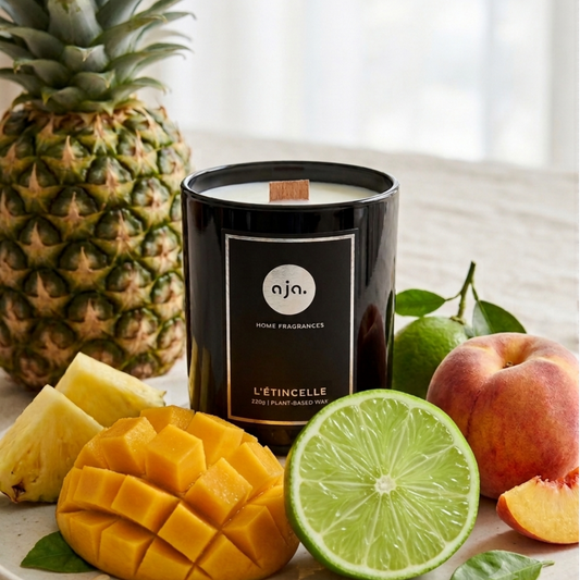 Candle labeled 'aia' surrounded by pineapple, mango, lime, and peach on a white surface.