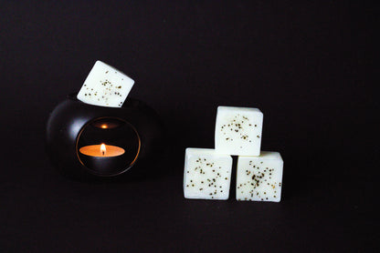 Black candle holder with a lit tealight creates a warm glow. Beside it, three white wax cubes with dried chamomile flower embedded on it