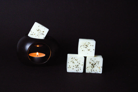 Black candle holder with a lit tealight creates a warm glow. Beside it, three white wax cubes with dried chamomile flower embedded on it
