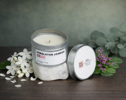 Candle with packaging on a wooden surface with flowers and eucalyptus leaves.