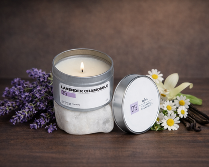 Candle in a decorative tin with lavender, chamomile flowers, and vanilla on a wooden surface.