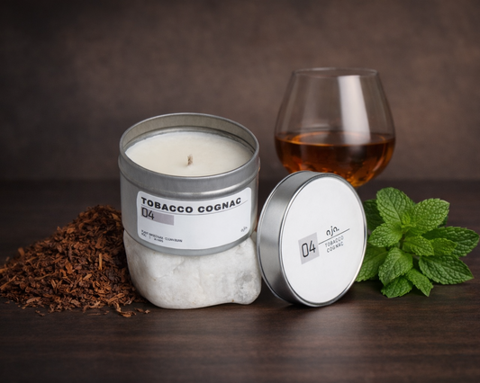 Candle labeled 'Tobacco Cognac' with a glass of liquid and mint leaves on a dark surface.