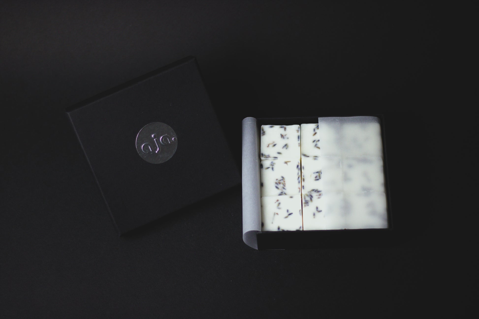 
A black box with a silver logo contains botanical wax melt cubes.
