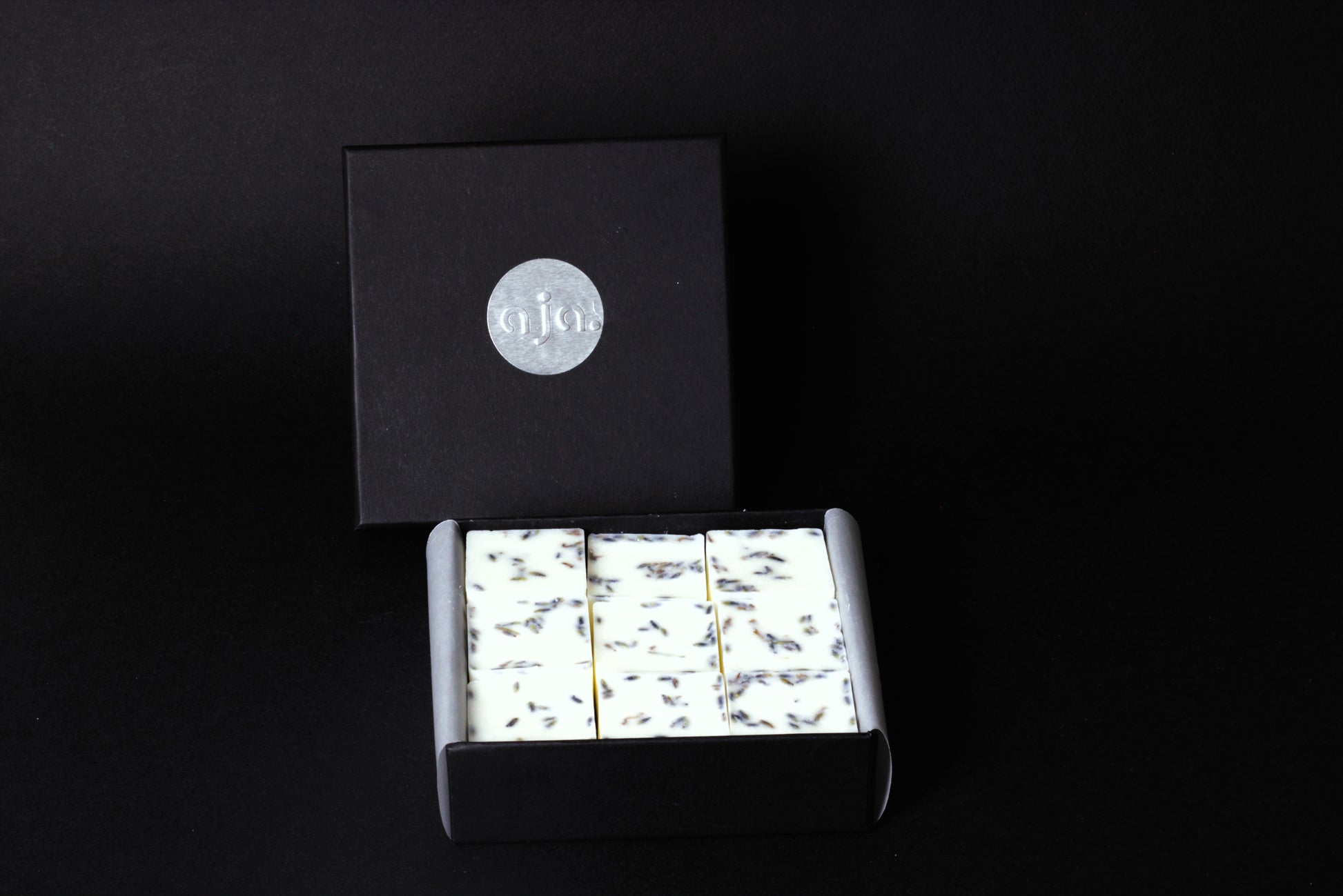 A black box with a silver logo contains botanical wax melt cubes.
