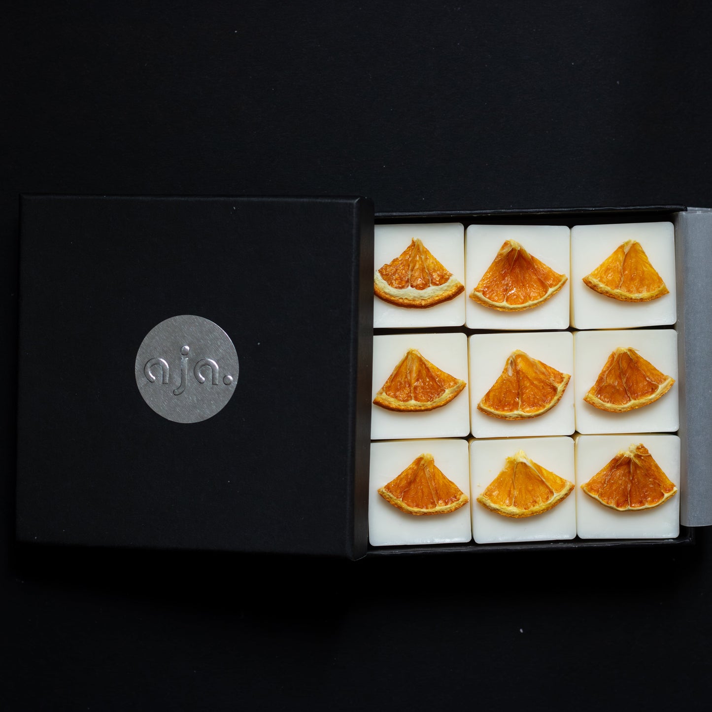 Box of botanical wax melts with orange slices on a black background