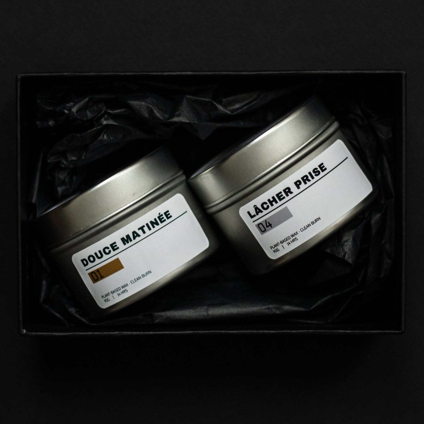 Two tins labeled 'Douce Matinee' and 'Lacher Prise' in a dark box on a black background. Ritual Candles for Productivity and Unwinding