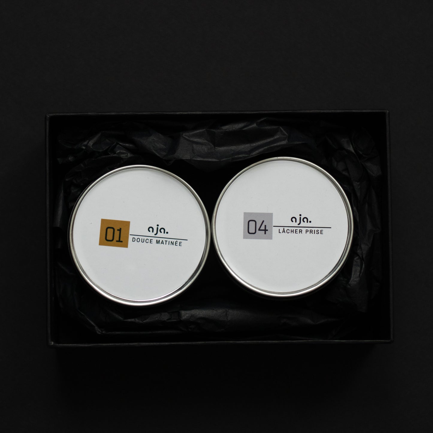 Two round containers with labels on a black background. Sweet Gourmand  and Woody Scent  Sets of Scented Candle
