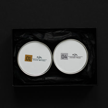 Two round containers with labels on a black background. Sweet Gourmand  and Woody Scent  Sets of Scented Candle