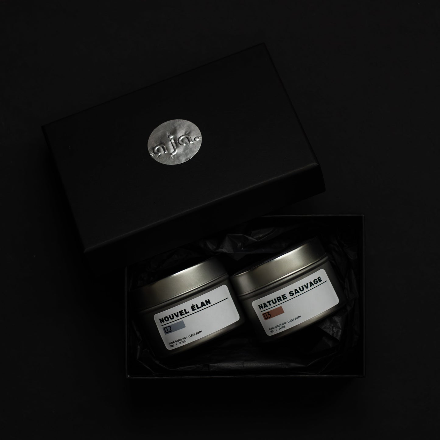 Two small containers in a black box with a visible brand logo on a dark background. A duo set collection for reset and mental clarity. Scented candle with floral and fresh scent.