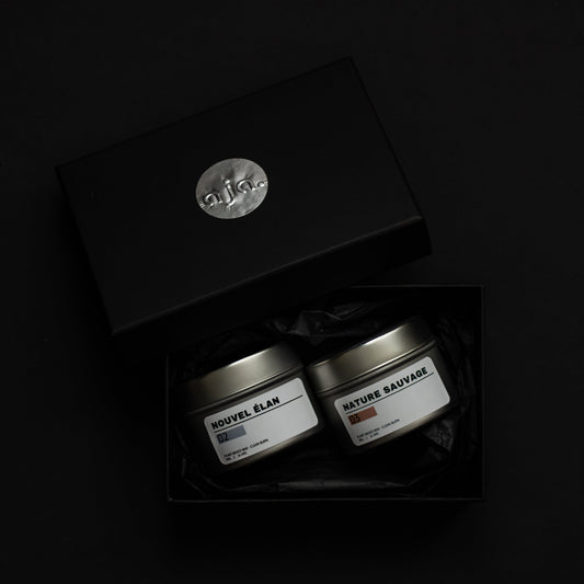 Two small containers in a black box with a visible brand logo on a dark background. A duo set collection for reset and mental clarity. Scented candle with floral and fresh scent.