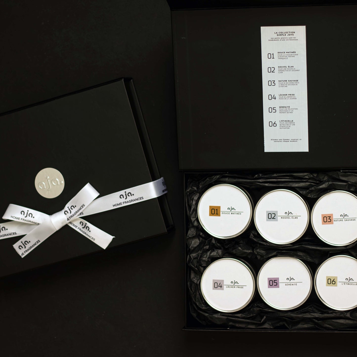 Set of six white candles in a black box with a decorative bow, on a dark background.