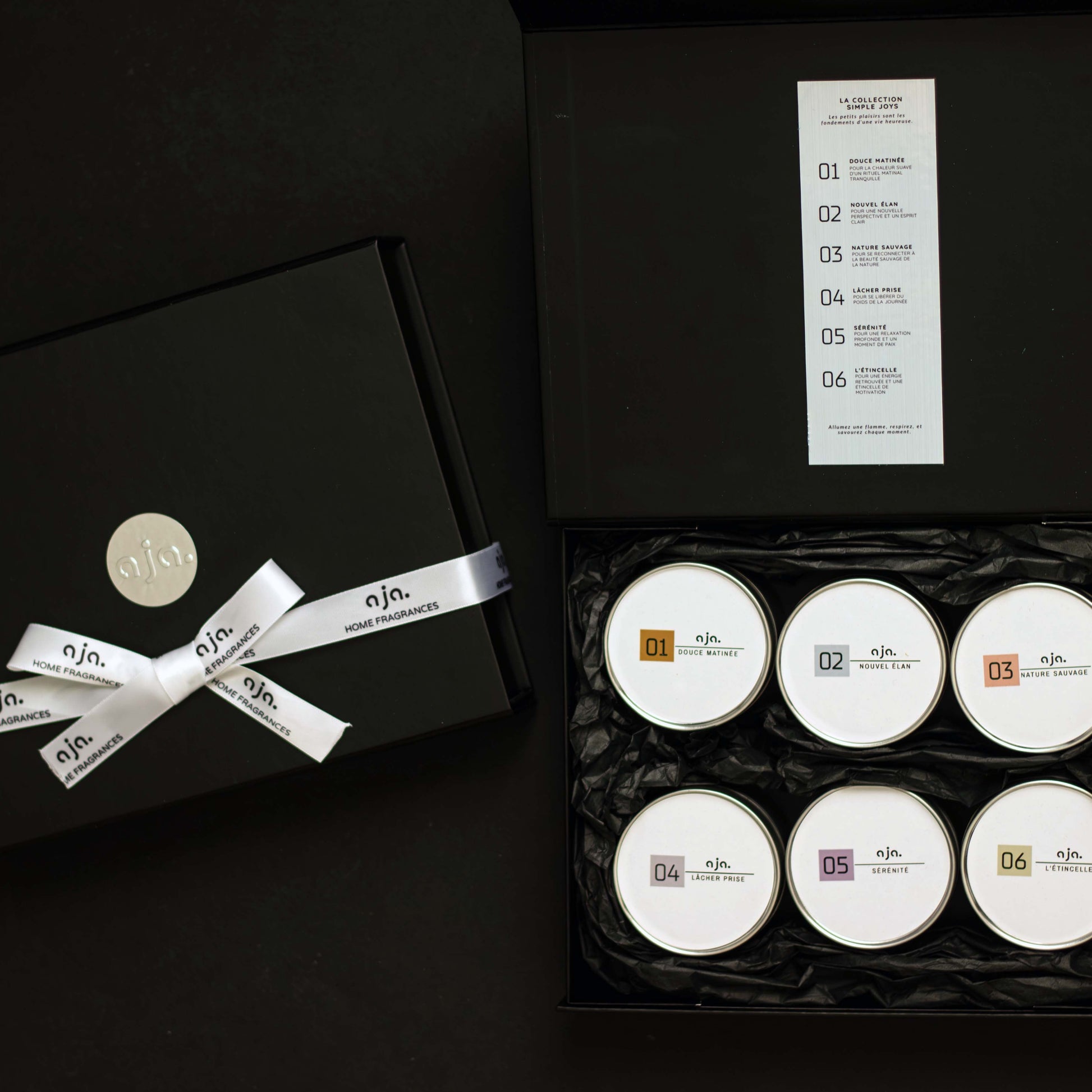 Set of six white candles in a black box with a decorative bow, on a dark background.