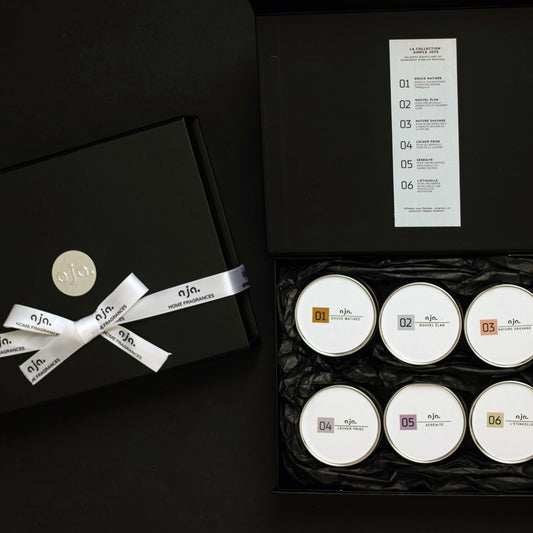 Set of six white candles in a black box with a decorative bow, on a dark background.