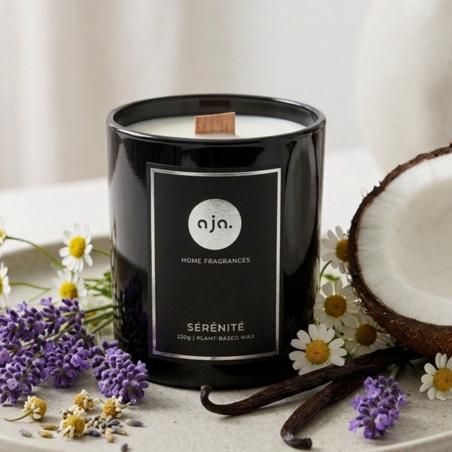 Black candle labeled 'aia Home Fragrances' with flowers and a coconut on a light surface.